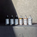 Row of Maison Margiela replica perfume bottles on a textured surface with a gray background