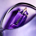 Purple Mugler Alien Refillable Eau de Parfum 60ml perfume bottle with gold accents, a matching purple bag and background