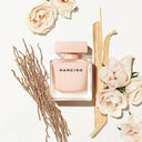 Narciso pink perfume bottle surrounded by flowers and dried plants on a light background