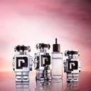 Three robot shaped Paco Rabanne Phantom Eau de Toilette 50ml bottles and a refill bottle with a reflective surface and gradient pink background