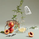 Tea cup with peach slices, vanilla beans, and a deer figurine on a light background