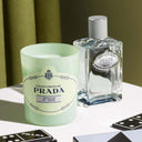 Prada Infusion De Cèdre Candle 165g and perfume bottle on a table with a green background
