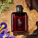 Red Ralph Lauren perfume bottle with a brand logo on a textured background with plants and wood.