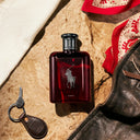 Ralph Lauren Polo Red Parfum 125ml perfume bottle on a textured surface with a keychain and leather jacket