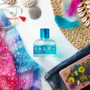 Ralph Lauren Ralph Eau de Toilette 50ml perfume bottle surrounded by colorful scarf, shell, and feather on a white background