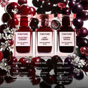 Three Tom Ford Cherry perfumes surrounded by cherries and flowers on a reflective surface with scent descriptions below each bottle.
