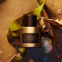 Tom Ford Oud Minérale Eau de Parfum 50ml perfume bottle on a textured surface with green seaweed and wood elements.