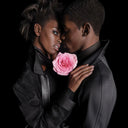 Two people embracing with a pink rose against a black background