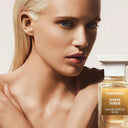 Woman with back sleek blonde hair looking into the lens with a Tom Ford White Suede Eau de Parfum 100ml bottle in bottom right corner