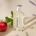 Clear glass Tommy Hilfiger Tommy Eau de Toilette 200ml perfume bottle with silver cap labeled 'tommy' next to a red apple on a light surface.