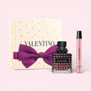 Valentino Donna Born In Roma Eau De Parfum Intense 50ml perfume and a travel sized penspray with a gift box featuring a purple bow on a light pink background