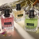 Three Valentino Born in Roma perfume bottles in pink, white, and green on a textured surface with lavender in the background.