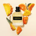 Valentino Uomo Born In Roma Yellow Dream Eau de Toilette 50ml perfume bottle surrounded by pineapple and orange slices on a beige background