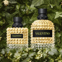 Two Valentino Uomo Born In Roma Yellow Dream Eau de Toilette perfume bottles with a textured design on a green leafy background