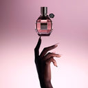 Hand pointing to a Viktor & Rolf Flowerbomb Eau de Parfum perfume bottle against a pink gradient background