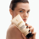 Woman holding a tube of YSL Yves Saint Laurent Libre Body Balm 200ml with a plain background